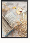 Een open boek, getiteld 'AMERICAN VOICES', ligt op een stoffen oppervlak naast schijfjes citroen en een doorzichtige fles met daarin een lichtgele vloeistof. Fijne takjes gedroogde bloemen zijn verspreid over de items, waardoor een zachte en serene compositie ontstaat, die doet denken aan een kunstzinnige wanddecoratie-display van CollageDepot genaamd "Ontspannen met een boekschilderij.