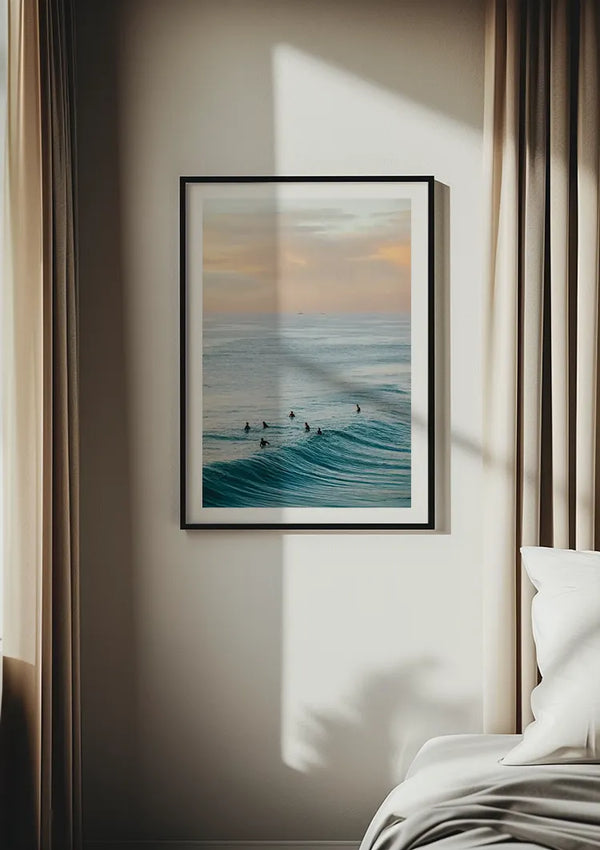 Aan een beige muur tussen twee beige gordijnen hangt een ingelijste foto van surfers die op de golven rijden. Dit boeiende stukje wanddecoratie, Zwemmen In De Wilde Zee Schilderij van CollageDepot, legt de oceaan vast bij zonsondergang. Het frame is rechthoekig met een eenvoudige zwarte rand, en in de rechter benedenhoek is een deel van een wit bed zichtbaar, moeiteloos bevestigd met een magnetisch ophangsysteem.,Zwart