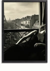 Een zwart-witfoto toont een persoon die achterover leunt bij een raam met uitzicht op een Parijse straat met de Eiffeltoren in de verte. De persoon is gekleed in een formele zwarte outfit, wat bijdraagt aan de vintage en verfijnde sfeer van dit Balkonzicht schilderij van CollageDepot, perfect voor wanddecoratie.