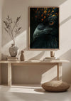 Een ingelijst CollageDepot Illuminating Black Bird Schilderij wordt tentoongesteld op een houten tafel tegen een lichtgekleurde muur. Op de tafel staan ook vazen en kleine decoratieve voorwerpen. Voor de tafel ligt een geweven kussen op de grond en links staat een tak in een vaas.,Lichtbruin