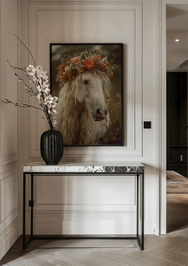 Aan een lichtgekleurde wand met lambrisering hangt een ingelijste foto van een wit paard met een bloemenkroon. Daaronder staat de aab 213 AI van CollageDepot, een consoletafel met marmeren blad en een zwarte vaas met witte bloemen. De kamer heeft een minimalistische, elegante inrichting met houten vloeren, die eenvoud en verfijning perfect combineren.,Zwart