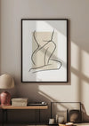 Een ingelijste minimalistische lijntekening van een zittende figuur, gemonteerd met een magnetisch ophangsysteem, hangt aan een beige muur. Daaronder staat een tafel met een geweven lamp, een stapel boeken, kaarsen en een decoratief item. Zonlicht werpt schaduwen op de muur en tafel, wat de elegante wanddecoratie van het Beige Vrouwenlichaam Schilderij van CollageDepot versterkt.,Zwart