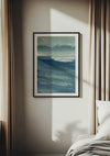 Een ingelijst CollageDepot Geschilderd blauwe zee schilderij hangt aan een muur tussen beige gordijnen, met behulp van een magnetisch ophangsysteem. Zonlicht werpt een schaduw over de muur en op een wit bed dat gedeeltelijk zichtbaar is aan de rechterkant van de afbeelding.