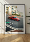 Een CollageDepot Ferrari 488 Pista Monaco schilderij met een ingelijste foto van een Ferrari 488 Pista met gouden wielen geparkeerd op straat staat tegen een witte muur. De achtergrond bestaat uit moderne woongebouwen en zonlicht werpt schaduwen op de muur en de houten parketvloer.,Zwart