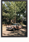 Een CollageDepot Roze Vintage Auto Schilderij wordt tentoongesteld in een straatbeeld met bomen en huizen. Het schilderij toont de auto in de schaduw van een grote boom met groene bladeren, en zonlicht filtert door de takken en werpt gevlekte schaduwen op de auto en de straat.,Zwart-Zonder,Lichtbruin-Zonder,showOne,Zonder