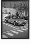 Een zwart-witfoto van drie personen die naast een geparkeerde vintage Porsche 911 Turbo op een parkeerplaats staan. De auto staat naast een zebrapad. Op de achtergrond staat nog een soortgelijke auto geparkeerd. Op de achtergrond zijn bomen en een hek te zien, perfect voor wanddecoratie met een magnetisch ophangsysteem van CollageDepot met het Klassieke Porsche 911 Turbo Schilderij.,Zwart-Zonder,Lichtbruin-Zonder,showOne,Zonder