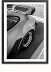 Een zwart-witfoto van de achterhoek van een Porsche Carrera, waarop een grote achterspoiler, de achterruit, een deel van het dak en een van de achterwielen te zien zijn. De auto staat geparkeerd op een verharde ondergrond naast een stoeprand aan de rechterkant van de afbeelding - perfect als wanddecoratie met een magnetisch ophangsysteem. Dit product staat bekend als Porsche Carrera Side View Schilderij van CollageDepot.,Zwart-Met,Lichtbruin-Met,showOne,Met