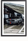 Een Zilveren Ford Mustang Schilderij van CollageDepot met witte, blauwe en rode racestrepen staat geparkeerd in een overdekte garage. De scène lijkt deel uit te maken van een autoshow of een racevoorbereidingsgebied, met vrachtwagens en uitrusting zichtbaar op de achtergrond, net als een kunstwerk zonder boren.,Zwart-Met,Lichtbruin-Met,showOne,Met