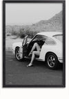 Een zwart-witfoto van een witte vintage auto geparkeerd op een verlaten weg met de bestuurdersdeur open. Er wordt een persoon met benen en schoenen met hoge hakken uit de auto gezien, maar zijn bovenlichaam is niet zichtbaar. Perfect als wanddecoratie, dit beeld vangt een mysterieus woestijnlandschap op de achtergrond. Dit is het **Porsche With Love Schilderij** van **CollageDepot**.,Zwart-Zonder,Lichtbruin-Zonder,showOne,Zonder