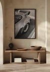 Een houten consoletafel tegen een lichtgekleurde muur met daarboven een Porsche Carrera Side View Schilderij van CollageDepot. Op de tafel staat een donkere vaas met een enkele steel, twee houten schalen en verschillende gestapelde boeken op de onderste plank. Zonlicht werpt schaduwen over het tafereel en versterkt de elegante wanddecoratie.,Zwart