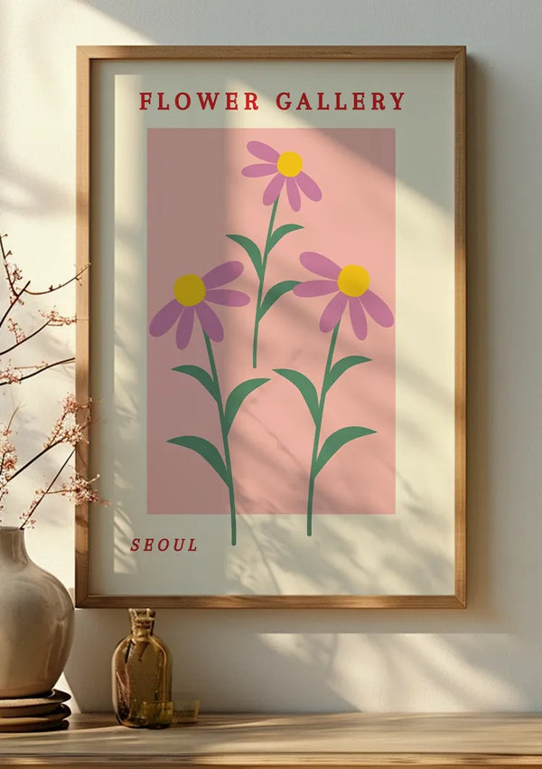 Een ingelijste poster met de titel "Flower Gallery" met gestileerde paarse bloemen met gele middelpunten op een roze achtergrond, weergegeven op een muur naast een vaas met kersenbloesems en een klein flesje bestsellers - CollageDepot.,Lichtbruin