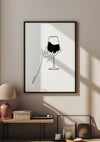 Een ingelijst stuk van CollageDepot's abstracte wijnglasschilderij met een hand die een wijnglas vasthoudt, wordt aan de muur gehangen met behulp van een magnetisch ophangsysteem. Onder het frame staat een tafel met een roze lamp, een geweven mand en nog een ingelijste foto. Zonlicht werpt schaduwen vanuit een raam op de muur en de tafel.,Zwart