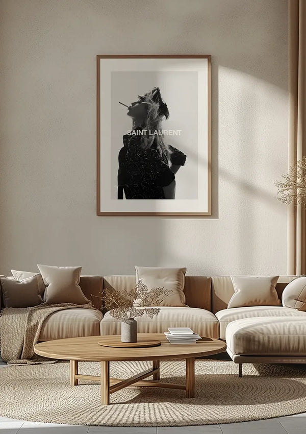 Een eigentijdse woonkamer met een groot stijlvol 'Saint Laurent' schilderij van CollageDepot, stijlvol ingelijst aan de muur. De kamer is voorzien van een beige bank, meerdere kussens en een ronde houten salontafel met gedroogd blad in een vaas. Een neutraal kleurenpalet domineert de ruimte.