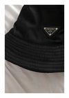 Een close-up van een zwarte CollageDepot-bucket hat met een opvallend driehoekig logoplaatje op posterpapier, wat het strakke ontwerp en de textuurdetails van de hoed benadrukt.-
