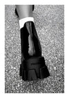 Een poster met ab 014 - zwart-wit van CollageDepot en toont de achterkant van iemands voet in een glanzend zwarte loafer met dikke zolen, die op een grindoppervlak stapt. De persoon draagt een witte sok.-