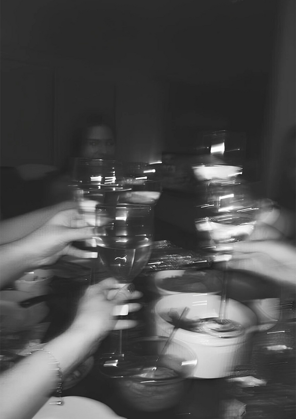 Een wazige CollageDepot ab 029 - zwart-wit kunstposter van mensen die met wijnglazen proosten boven een eettafel. De focus ligt op de bril, die een gevoel van beweging geeft. Er zijn borden en kommen zichtbaar op de tafel.-