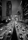 Poster van CollageDepot's ab 030 - zwart-wit afbeelding van een drukke stadsstraat 's nachts, met wazige bewegingen van auto's op een meerbaansweg geflankeerd door hoge gebouwen verlicht door stadslichten.-