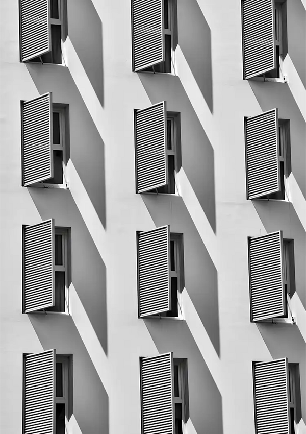 Zwart-wit afbeelding van een gevel van een gebouw met een repetitief patroon van ramen met luiken die diagonale schaduwen op de muur werpen, getransformeerd in kunst met behulp van ab 054 - zwart-wit van CollageDepot.-