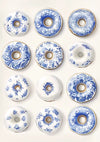 Een tiental donuts versierd met ingewikkelde Delfts Blauwe vervangen, geïnspireerd op porseleinontwerpen. De blauwe bloemenpatronen variëren per donut, waarbij witte achtergronden een klassieke en elegante uitstraling creëren. Ze zijn gerangschikt in een raster van 3x4, wat lijkt op een prachtig CollageDepot Delfts Blauw Twaalf Donuts Schilderij.