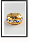 Op een ingelijst schilderij is een hamburger te zien met een broodje dat van glanzend goudkleurig materiaal lijkt te zijn gemaakt. Tussen de broodjes zit, in plaats van een traditioneel vleespasteitje, een decoratief stuk blauw en wit porselein. Dit unieke kunstwerk speelt zich af tegen een effen witte achtergrond met een optioneel magnetisch ophangsysteem. Het product heet Delfts Blauw Gouden Hamburger Schilderij van CollageDepot.,Zwart-Met,Lichtbruin-Met,showOne,Met