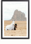 Een ingelijste afbeelding van een wit en bruin paard staande in een woestijnlandschap. Het ene paard is wit en het andere paard is bruin met zwarte manen. De achtergrond toont een grote rotsformatie onder een bewolkte hemel. Perfect als wanddecoratie met zijn magnetisch ophangsysteem voor eenvoudige weergave, het Paarden in Landschap Schilderij van CollageDepot.,Zwart-Met,Lichtbruin-Met,showOne,Met