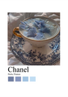 Elegant porseleinen theekopje met gouden rand op een bijpassend schoteltje, beide met blauwe bloemmotieven. De beker bevat water met blauwe hortensiablaadjes. Hieronder zijn het woord "bb 006 - fashion" en "Paris, France" gedrukt met een palet van blauwtinten.-
