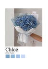 Een boeket blauwe gipskruidbloemen, verpakt in wit papier met een wit lint, vastgehouden door een persoon tegen een effen achtergrond. De tekstoverlay luidt "Chloé Paris Schilderij, CollageDepot" met vier blauwe kleurstalen onderaan, die de serene schoonheid van elegante wanddecoratie oproepen.-