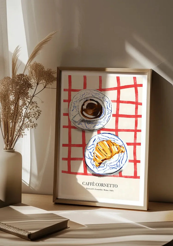 Een ingelijste print van een gestileerde illustratie met een kopje koffie en een croissant op een rood geruit tafelkleed. De print draagt de tekst "Café Cornetto, Firenze & Venezia / Rome / Italia" en wordt naast een vaas met gedroogd bloemstuk geplaatst, waardoor het een ideale wanddecoratie is in combinatie met een magnetisch ophangsysteem. Dit is het Café Cornetto Schilderij van CollageDepot.,Lichtbruin