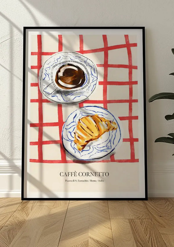 Op een ingelijste poster op de vloer is een illustratie te zien van een koffiekopje en een croissant op een rood geruit tafelkleed, met het opschrift 'Café Cornetto' en de aanvullende tekst 'Piazza di Trevi/Roma/Italia'. Het CollageDepot Café Cornetto Schilderij wordt versterkt door de bladeren van een plant die gedeeltelijk zichtbaar zijn aan de rechterkant.,Zwart