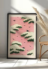 Een ingelijst schilderij Roze lucht van CollageDepot leunt tegen een witte muur, met een dessin van groene en witte wolken tegen een roze lucht met vliegende zwarte vogels. Rechts zijn een deel van een rieten stoel en een hoge gedroogde plant zichtbaar. Zonlicht werpt schaduwen op de vloer, wat de serene Japanse stijl versterkt.
