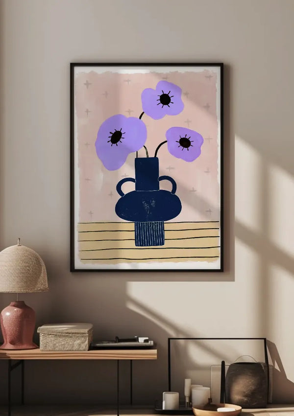 Een ingelijste Lavendelbloemen in Vaas Schilderij van CollageDepot hangt aan een beige muur, met behulp van een magnetisch ophangsysteem. Het schilderij staat boven een plank met een roze lamp, een beige geweven doos, een witte kaars en andere decoratieve voorwerpen. Licht filtert door het raam en werpt schaduwen op de muur.,Zwart
