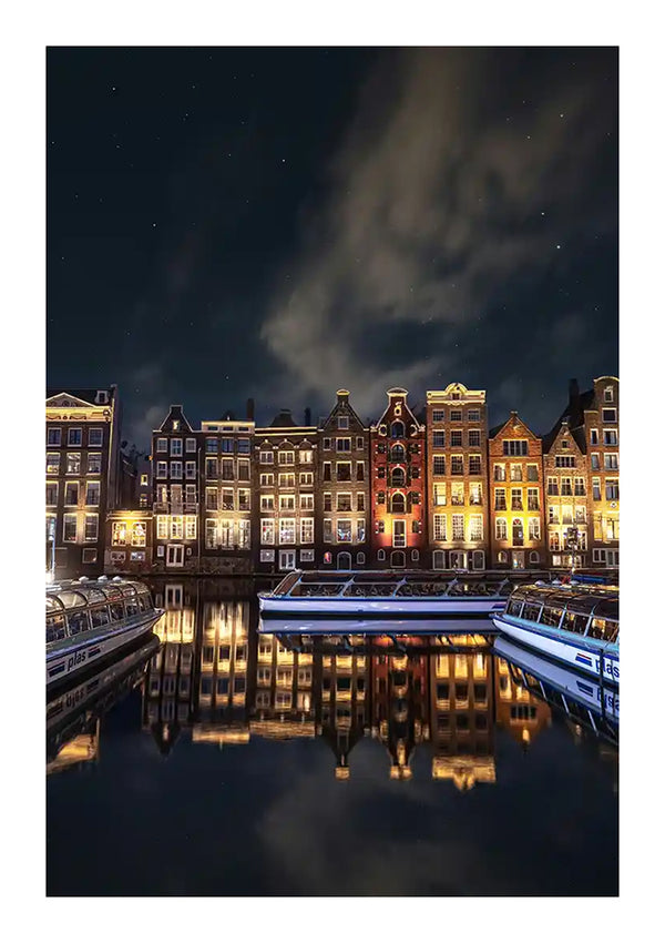 Een nachtelijk zicht op een gracht in een stad, met verlichte traditionele Amsterdamse grachtenpanden. Reflecties van de gebouwen en verschillende boten zijn zichtbaar in het kalme water beneden, met een gedeeltelijk bewolkte hemel en verspreide sterren erboven, waardoor een serene achtergrond ontstaat die perfect is voor het wanddecor Amsterdamse Grachtenpanden Schilderij van CollageDepot.-