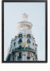 Ingelijste foto van een wit gebouw met meerdere verdiepingen, sierlijke architectuur en een cilindrische toren bovenaan. Het gebouw heeft meerdere balkons met zwarte balustrades. Op de zijkant van het gebouw is een geel kroonlogo met het woord "Rolex" zichtbaar, perfect als CollageDepot Rolex-winkel Madrid schilderij wanddecoratie.