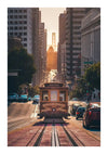 Een vintage tram rijdt een steile heuvel af in een stedelijk gebied met aan weerszijden hoge gebouwen. Er rijden auto's naast de tram. De zon gaat onder en werpt een warme gloed over het tafereel. Op het straatnaambord staat "Van Ness Ave" in San Francisco, wat een perfecte scène creëert voor Tram San Francisco Schilderij van CollageDepot.-