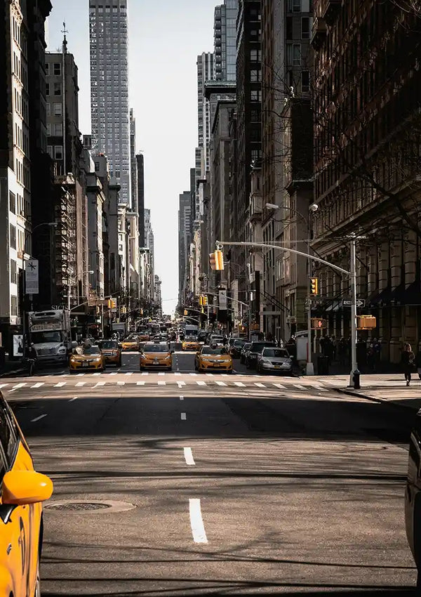 Een stadsstraat met hoge gebouwen aan beide kanten, gele taxi's en andere voertuigen op de weg, voetgangers zichtbaar op de trottoirs en verkeerslichten op de kruising. De sfeer lijkt rustig met minimaal verkeer, net zoals een Taxi's in New York Schilderij van CollageDepot dat het dagelijks leven vastlegt als een vorm van wanddecoratie.
