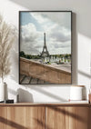 Ingelijst Uitzicht Op De Eiffeltoren Schilderij van CollageDepot opgehangen aan een muur boven een houten dressoir met behulp van een magnetisch ophangsysteem. Op het dressoir staan decoratieve voorwerpen, waaronder een vaas met pampasgras, een keramieken bakje en twee boeken. De kamer wordt verlicht door natuurlijk licht.,Zwart