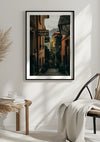 Een ingelijst Bellagio Italië schilderij van CollageDepot van een smal, geplaveid steegje tussen gele en oranje gebouwen, versierd met groen, op een witte muur. Aan de rechterkant staat een rieten stoel met een gedrapeerde witte deken, en aan de linkerkant staat een kruk met strotextuur en een open boek. Deze charmante wanddecoratie is voorzien van een magnetisch ophangsysteem voor eenvoudige presentatie.