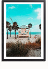 Een ingelijste foto, die doet denken aan een Badmeestertoren Op Het Strand Schilderij van CollageDepot, toont een zonnig strandtafereel met een kleine, lichtgekleurde badmeesterpost in het midden, omgeven door palmbomen. Mensen loungen op het zand en de oceaan is zichtbaar op de achtergrond onder een helderblauwe lucht - perfect als wanddecoratie met een eenvoudig magnetisch ophangsysteem.,Zwart-Met,Lichtbruin-Met,showOne,Met