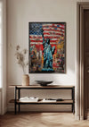 Aan een witte muur hangt een ingelijst Vrijheidsbeeld New York Schilderij van CollageDepot met het Vrijheidsbeeld tegen de achtergrond van de Amerikaanse vlag. Daaronder staat een houten consoletafel met een open boek, een decoratieve schaal en een vaas met gedroogde takken. Deze opvallende wanddecoratie is beveiligd met een magnetisch ophangsysteem.,Zwart