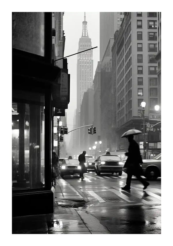 Een zwart-wit afbeelding van een regenachtige dag in een stad dient als perfecte wanddecoratie. Een persoon die een paraplu vasthoudt, steekt een natte straat over, met auto's en voetgangers omlijst door hoge gebouwen en het Empire State Building op de achtergrond. Verkeerslichten en straatverlichting zorgen voor subtiele verlichting, allemaal prachtig samengebracht door CollageDepot's Rainy Day Schilderij met een magnetisch ophangsysteem.-
