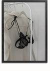 Een ingelijste foto, vormgegeven als opvallende wanddecoratie, toont kleding op hangers. Een wit kledingstuk en een zwarte kanten bh hangen aan een wit kledingrek tegen een effen achtergrond, waardoor een elegant en minimalistisch Lingerie op kledingrek schilderij van CollageDepot ontstaat.