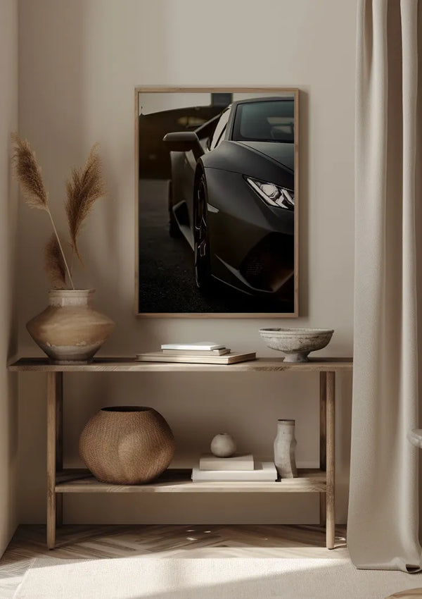 Het minimalistische interieur bestaat uit een consoletafel met diverse decoratieve items, zoals vazen, een geweven mand en een kommetje. Boven de tafel hangt het donkergrijze Lamborghini Huracan-schilderij van CollageDepot, waarop een deel van de koplamp en de zijspiegel te zien is.,Lichtbruin