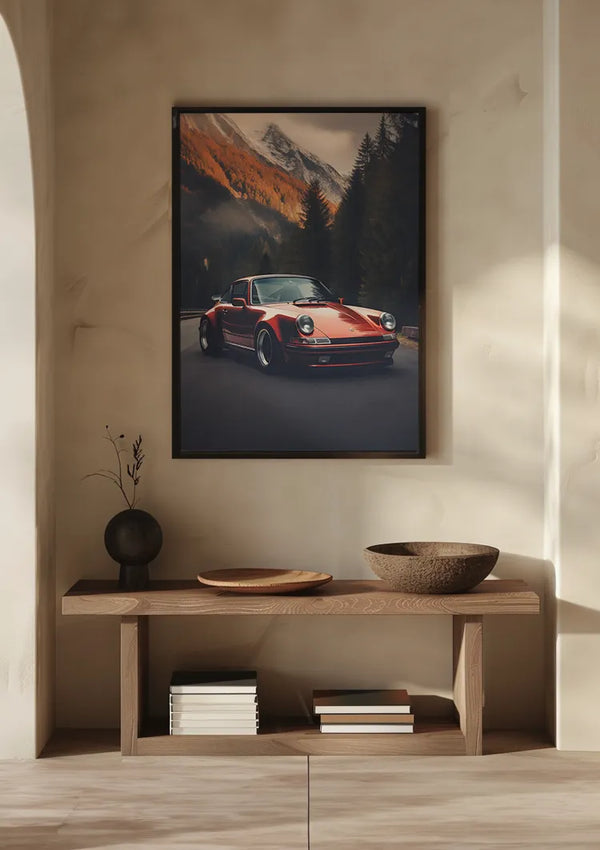 Op een houten plank tegen een beige muur staat een kleine tak in een donkere vaas, een platte schaal en een kom. Boven de plank, ingelijst als wanddecoratie, hangt het CollageDepot Porsche 911 On Tour Schilderij. Op de plank eronder staan een paar boeken netjes gestapeld.,Zwart