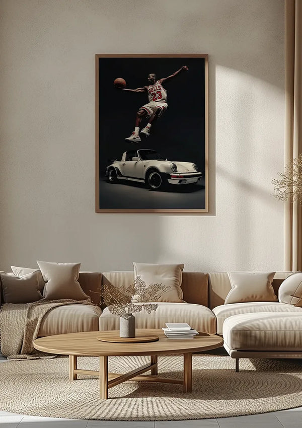 Een minimalistische woonkamer met een grote ingelijste poster van een basketbalspeler die met een bal over een klassieke 911 cabrio springt, aan de muur boven een beige bank. De kamer is voorzien van een ronde houten salontafel, lichtgekleurde kussens en een neutrale inrichting voor een elegante wanddecoratie zoals "The Dream Team Schilderij" van CollageDepot.,Lichtbruin