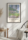 Een ingelijste poster van het schilderij Populieren van Claude Monet wordt met behulp van een magnetisch ophangsysteem onberispelijk aan een witte muur gehangen. Onder het schilderij staat de tekst "CLAUDE MONET" en "Populieren, roze effect | 1891." Aan de rechterkant staat een stoel met een deken erover gedrapeerd, en aan de linkerkant een houten tafel met boeken en een glas. Het Claude Monet Poplars, Pink Effect Schilderij van CollageDepot ziet er perfect uit in deze omgeving.,Zwart