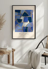 Aan de muur hangt een ingelijst CollageDepot P. Klee Blauwe Abstractie Schilderij met blauwe geometrische vormen en witte accenten, gebruikmakend van een magnetisch ophangsysteem. Onder het schilderij staat een tafeltje met een stapel boeken en een sierplant. Naast de tafel staat een stoel met een lichtgekleurde deken erover gedrapeerd.,Zwart