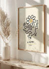 Een ingelijste K. Haring - Bloem Illustratie Schilderij van CollageDepot met een gestileerde figuur met een bloem als hoofd, gesigneerd "K. Haring" met de titel "Flower." Het frame, hangend via een magnetisch ophangsysteem, staat op een plank naast een witte vaas met gedroogde planten, alles tegen een zacht verlichte achtergrond.,Lichtbruin