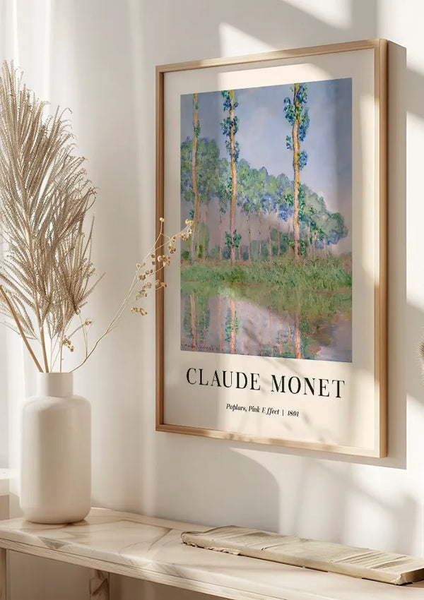 Een ingelijst schilderij van Claude Monet Poplars, Pink Effect van CollageDepot hangt aan een witte muur. Het schilderij toont hoge bomen, weerspiegeld in een watermassa. Een witte vaas met gedroogd blad staat op een nabijgelegen wit oppervlak, gedeeltelijk zichtbaar linksonder. Het magnetische ophangsysteem zorgt ervoor dat dit meesterwerk de perfecte wanddecoratie blijft.,Lichtbruin