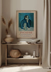 Een minimalistische kamer met een houten consoletafel tegen een beige muur. Op de tafel staan decoratieve voorwerpen, waaronder vazen, een kom en een mand. Boven de tafel hangt een CollageDepot Picasso 1954 Schilderij met een magnetisch ophangsysteem, gedateerd 9 juni tot 28 september 1954.,Lichtbruin