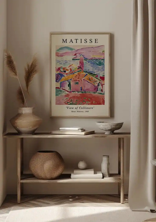 Het minimalistische interieur bestaat uit een rustieke houten tafel met een donkere vaas met gedroogd pampagras. Boven de tafel hangt een kleurrijk schilderij van H. Matisse 1905 van CollageDepot met behulp van een magnetisch ophangsysteem. Rechts staat een rotan stoel, naast een rond geweven tapijt en een rieten mand op een hardhouten vloer.,Zwart